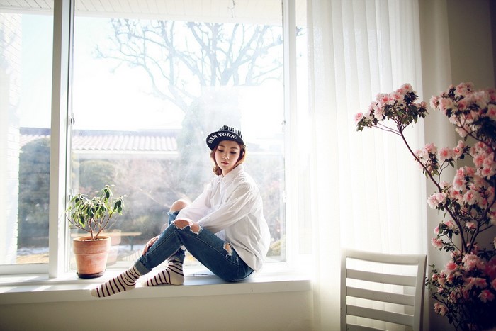 Asian woman in white shirt and ripped jeans sitting by window