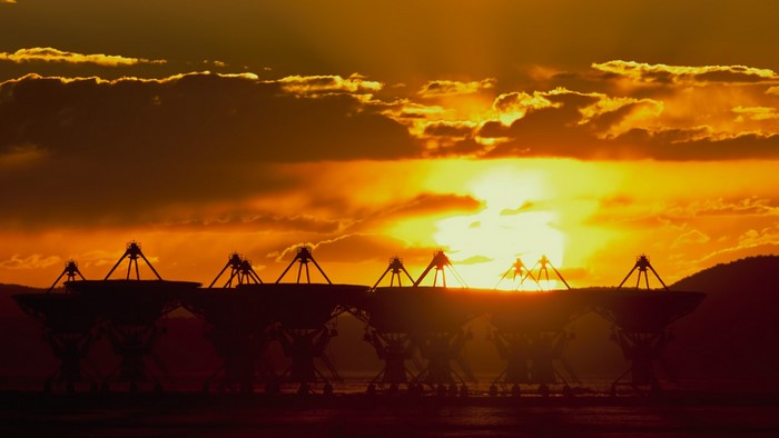 Radio telescopes silhouetted against a sunset