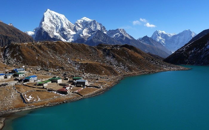 Village by turquoise lake with snow-capped mountains
