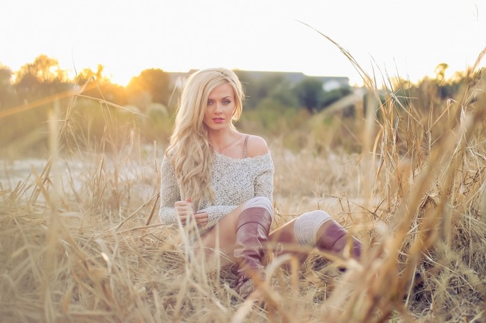 Woman in sweater and boots sitting in dry grass