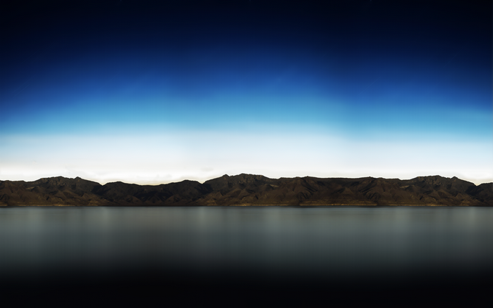 Mountain range reflected in a dark lake under a gradient sky