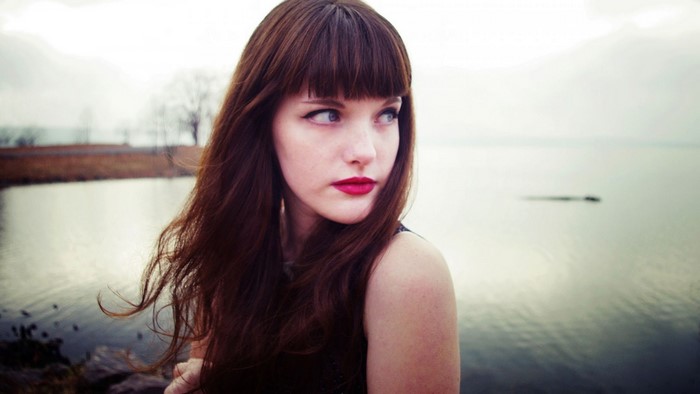 Woman with long brown hair and red lipstick by the water