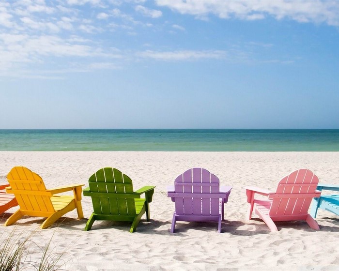 Colorful Adirondack chairs on a sandy beach by the ocean
