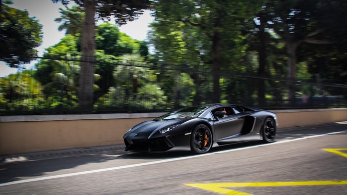 Black Lamborghini Aventador driving on a road