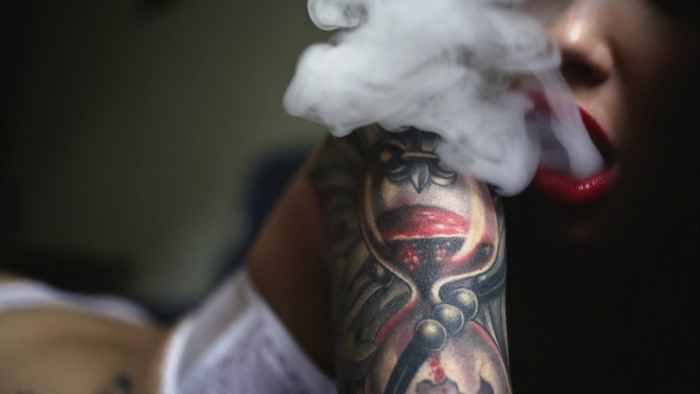 Woman with hourglass tattoo exhaling smoke