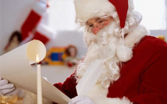 Santa Claus reading a scroll by candlelight