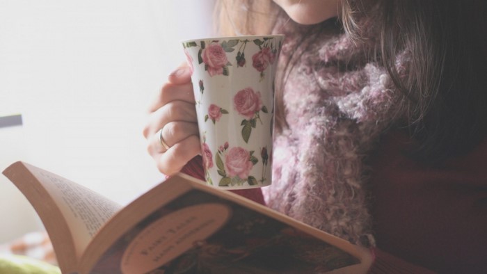 Woman reading a book and drinking from a floral mug