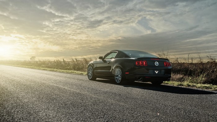 Black Ford Mustang GT driving on a road at sunset