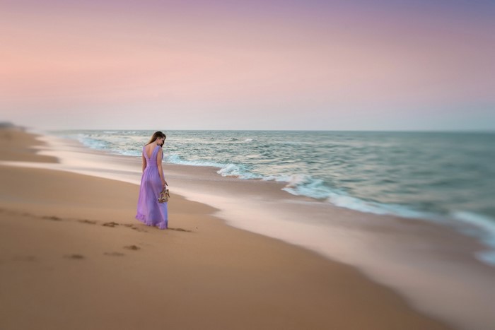 Woman in purple dress walking on beach at sunset