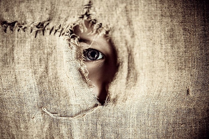 Child's eye peeking through torn burlap fabric
