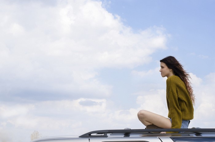 Woman sitting on car roof against sky