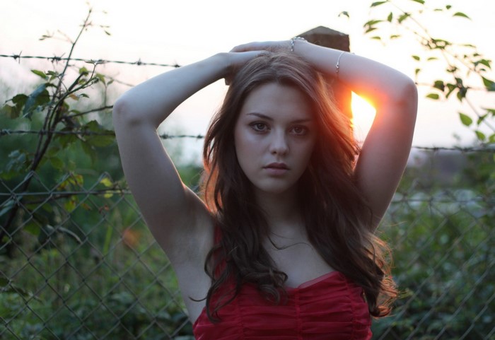 Woman in red dress with hands behind head at sunset