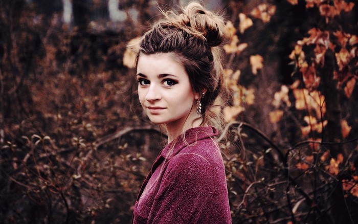 Woman with messy bun and purple jacket in autumn forest