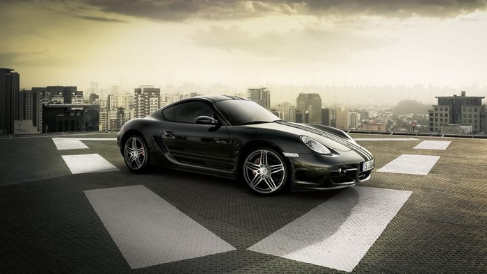 Black Porsche Cayman S on a helipad with city skyline