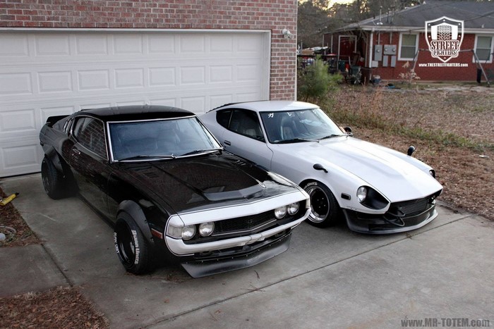 Two classic Japanese sports cars parked in front of a garage