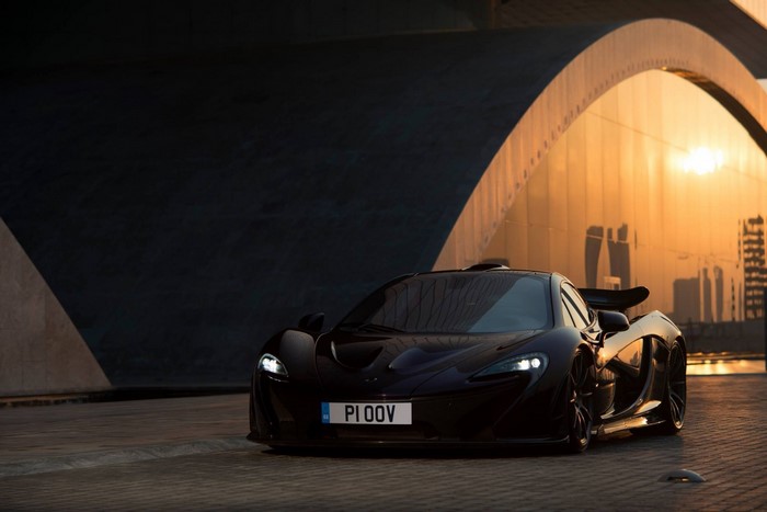 Black McLaren P1 supercar parked under a bridge at sunset