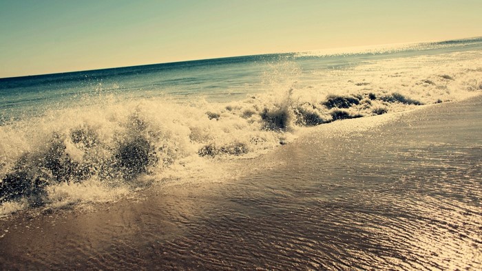 Ocean wave crashing on a sandy shore at sunrise
