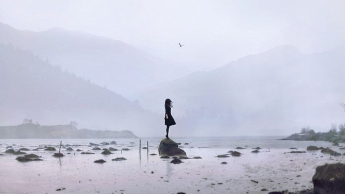 Woman standing on a rock in the sea with mountains in the background