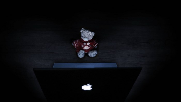 Teddy bear in front of a glowing Apple laptop