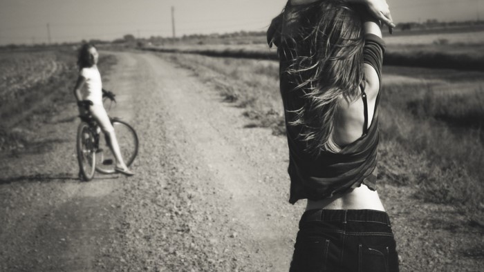 Woman in jeans and bra on a dirt road with a bicycle