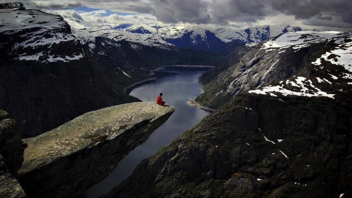 Person sitting on Trolltunga cliff overlooking a fjord in Norway