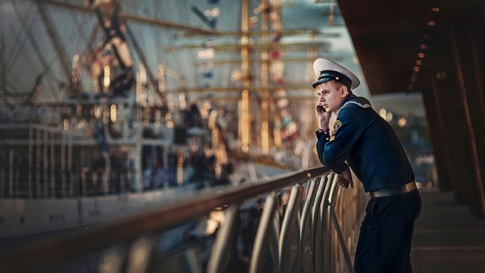 Sailor on a phone with a ship in the background