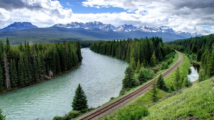 River and railway through a forest with mountains