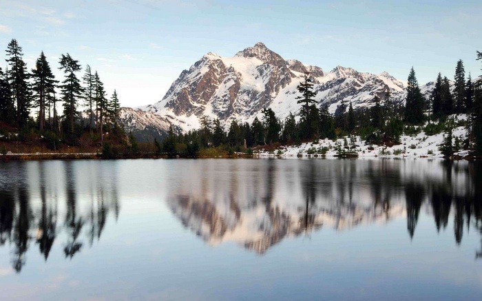 Snow-capped mountain reflected in a lake with pine trees
