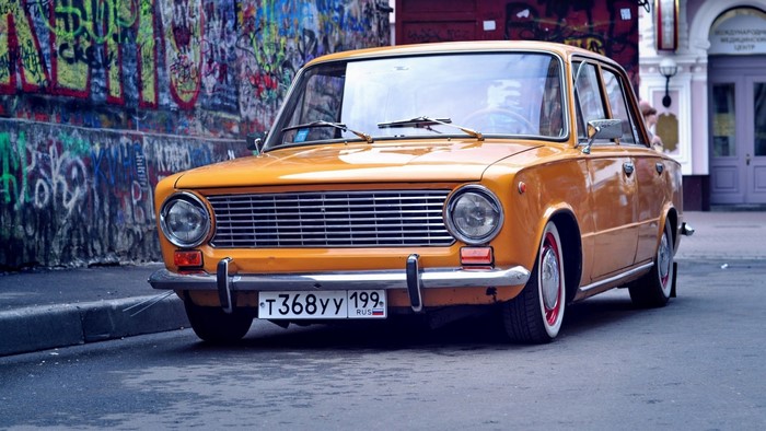 Orange vintage Lada car parked on a street with graffiti