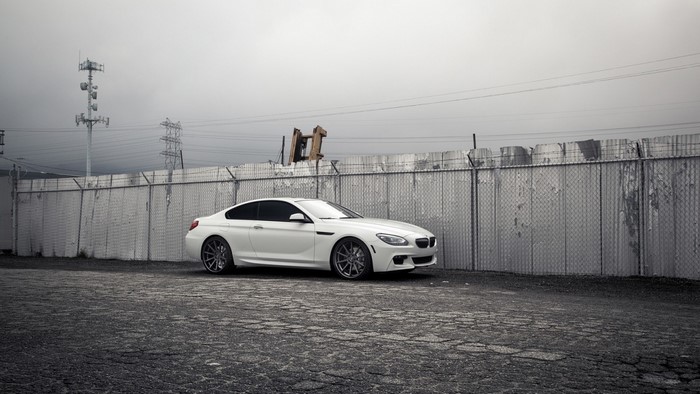 White BMW sports car parked by a chain-link fence