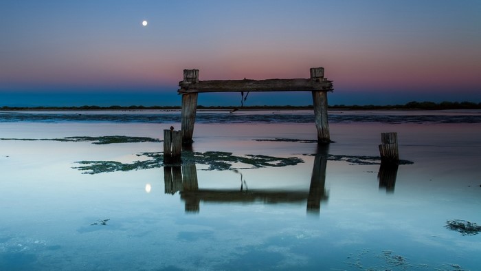 Wooden structure in water at dusk with moon