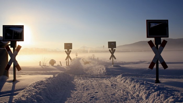 Snowy landscape with railway crossing signs at sunrise