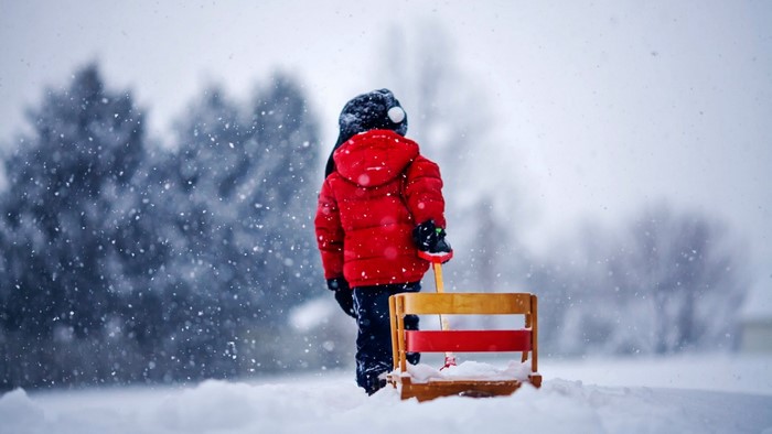 Child in red jacket pulling a sled in the snow