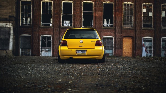 Yellow Volkswagen GTI parked in front of an abandoned brick building