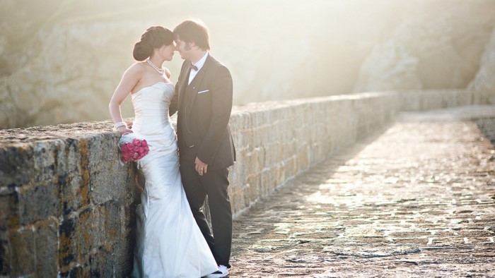 Bride and groom embracing by a stone wall