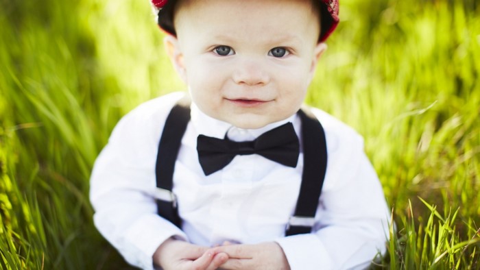 Baby boy wearing suspenders and bow tie in grass