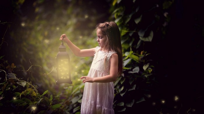 Little girl holding a lantern in a dark forest