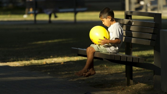 Boy sitting on a park bench with a yellow ball