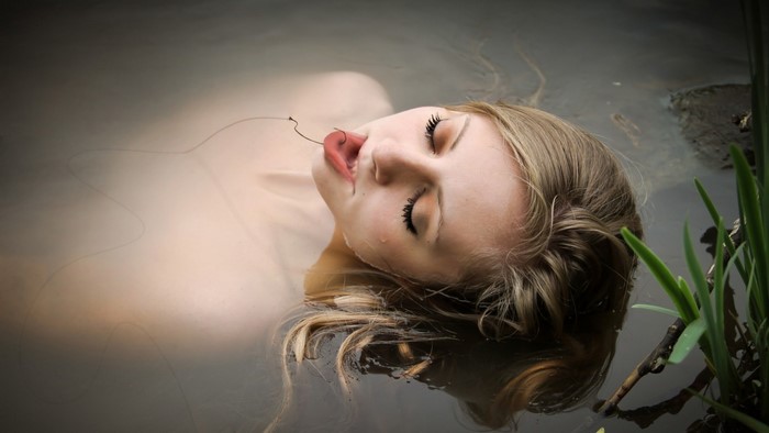 Woman lying in water with a twig on her tongue