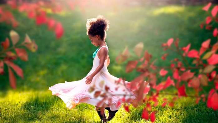 Young girl in a pink dress twirling in a sunlit meadow