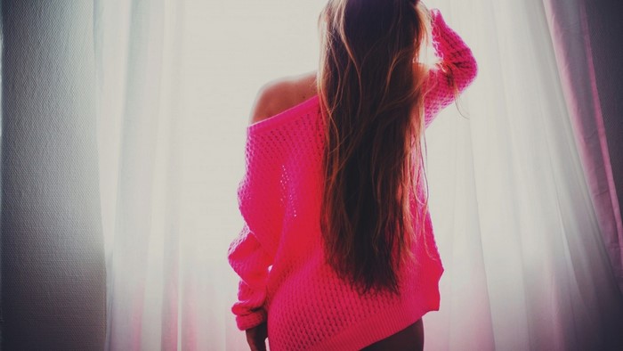 Woman in pink sweater with long hair by the window