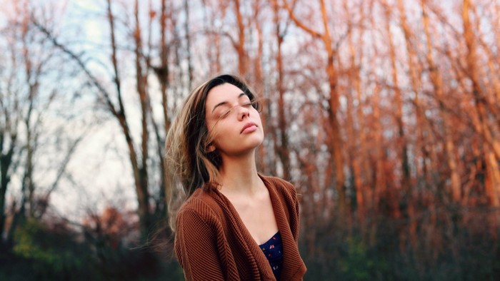Woman with eyes closed in a brown cardigan outdoors