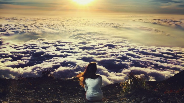 Woman sitting on a mountain above clouds at sunrise