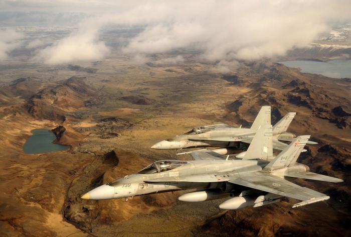Two Canadian CF-18 Hornets fly over a rugged landscape