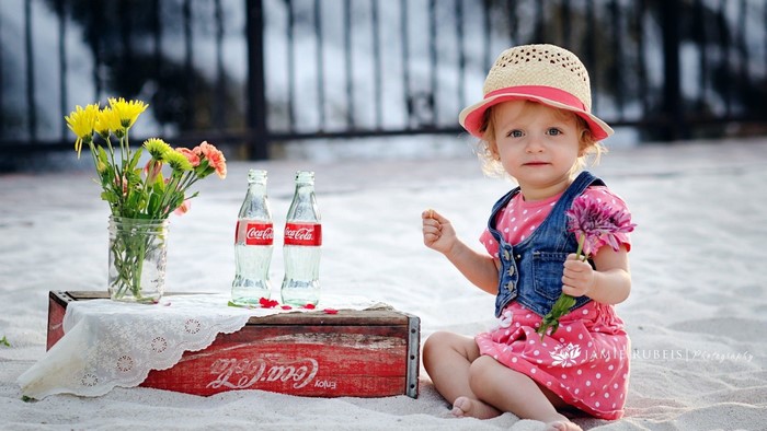 Toddler girl with Coca-Cola bottles and flowers on the beach