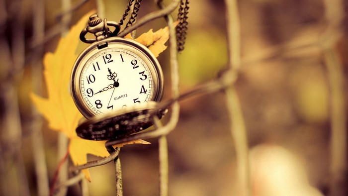 Pocket watch on a fence with autumn leaf