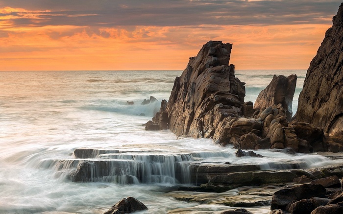 Ocean waves crashing on rocky shore at sunset