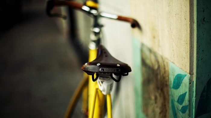 Yellow bicycle with Brooks saddle leaning on wall
