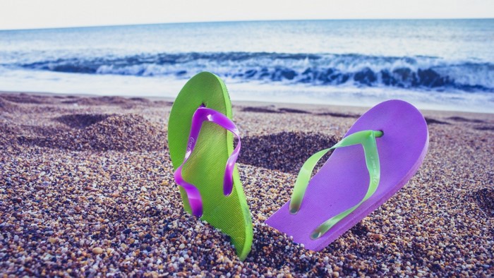 Green and purple flip flops on a beach