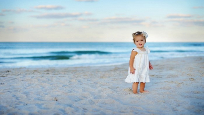 Little girl in white dress on a sandy beach by the ocean